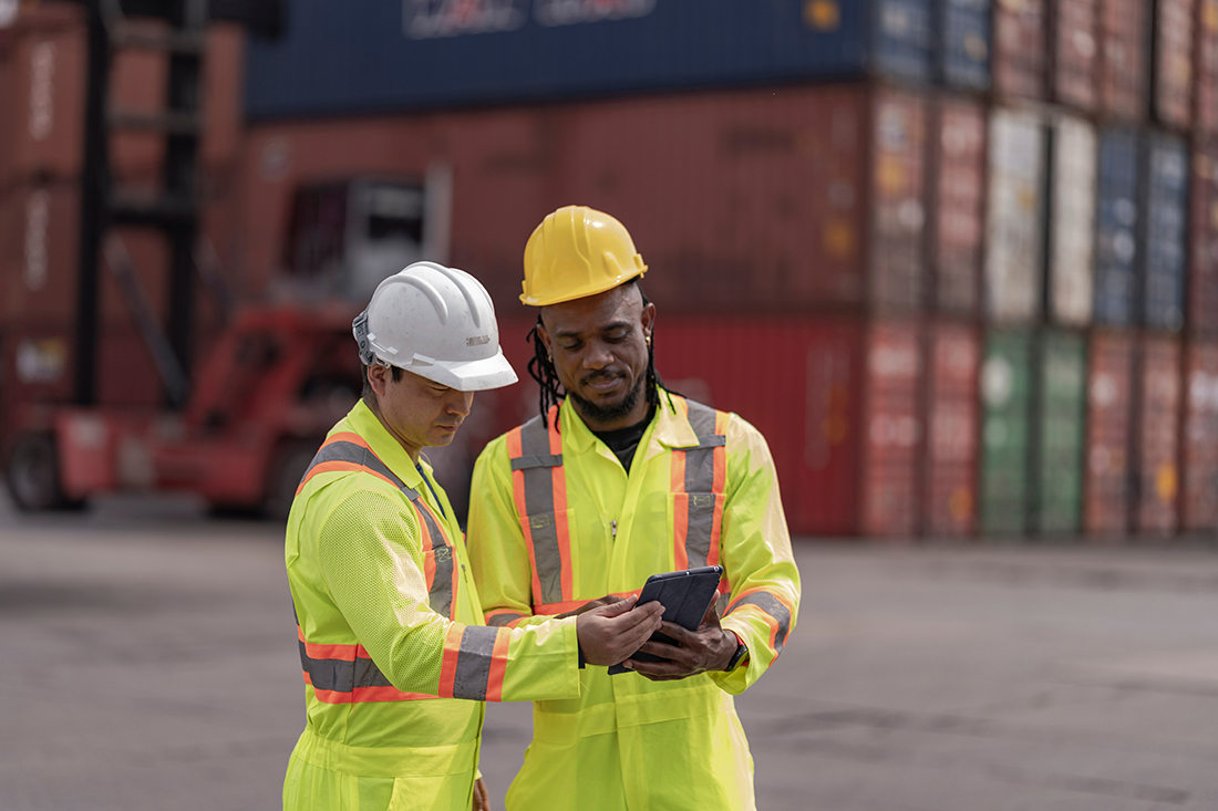 Employees in a dockyard review a tablet.