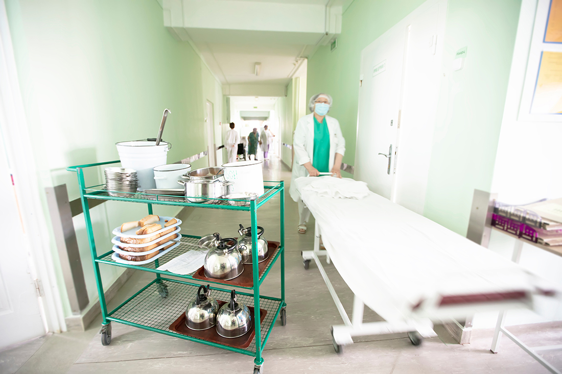 Hospital worker pushes a bed down the hallway with a meal cart.
