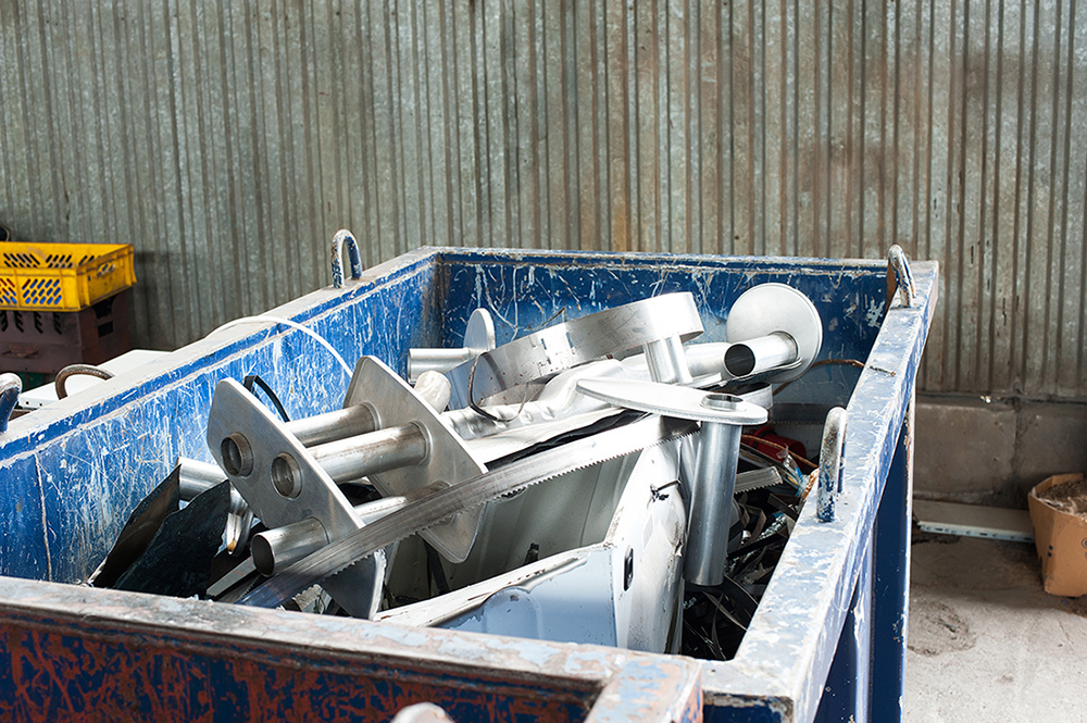 Metal waste components in a blue dumpster in an industrial area